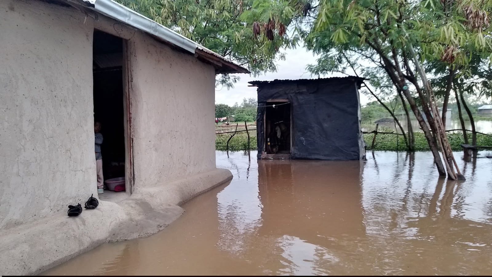 Community members navigating deep floodwaters near their collapsed homes
